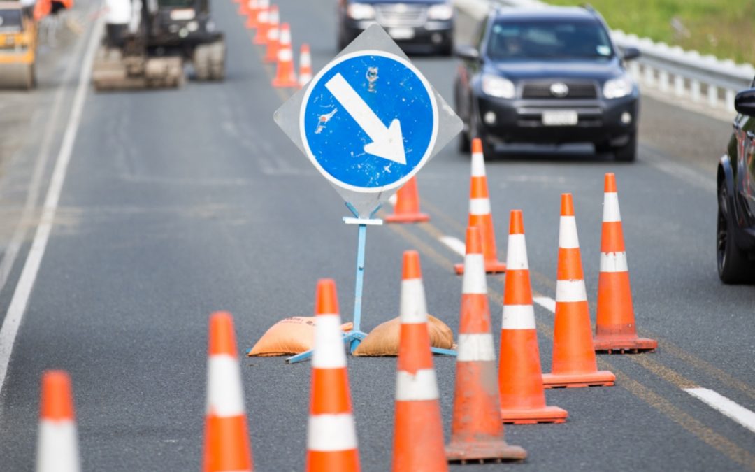 a Photo of a busy road lined with traffic cones splitting the road. There is a road sign clearly visible to all passing cars.