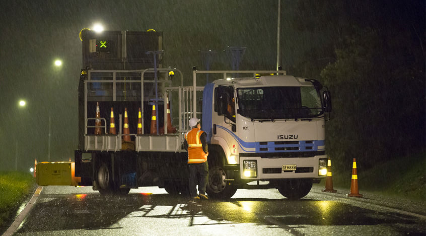 A photo of a truck being instructed by a temporary traffic expert. The rain is pouring and its night time